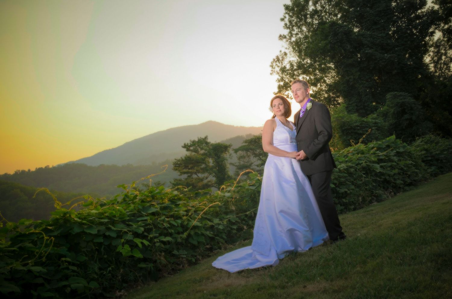 A couple in wedding attire stands on a hilltop at sunset as golden light illuminates the mountain landscape in Pigeon Forge TN.