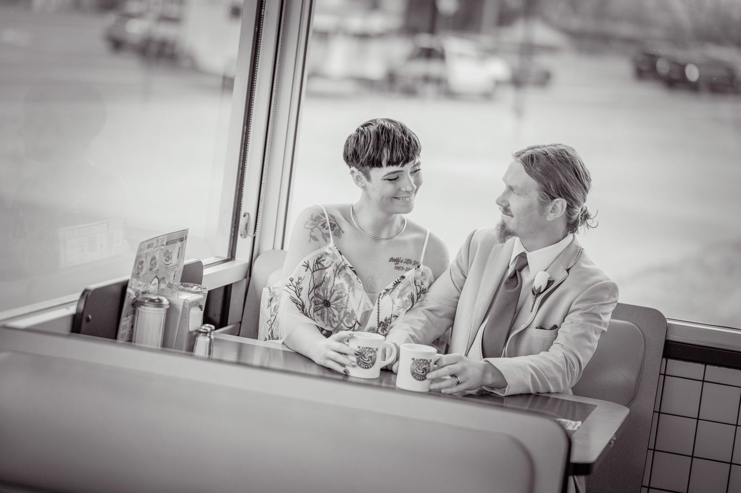 A couple in retro style wedding clothing share an intimate moment while dining at a vintage diner booth by the window at Waffle House.