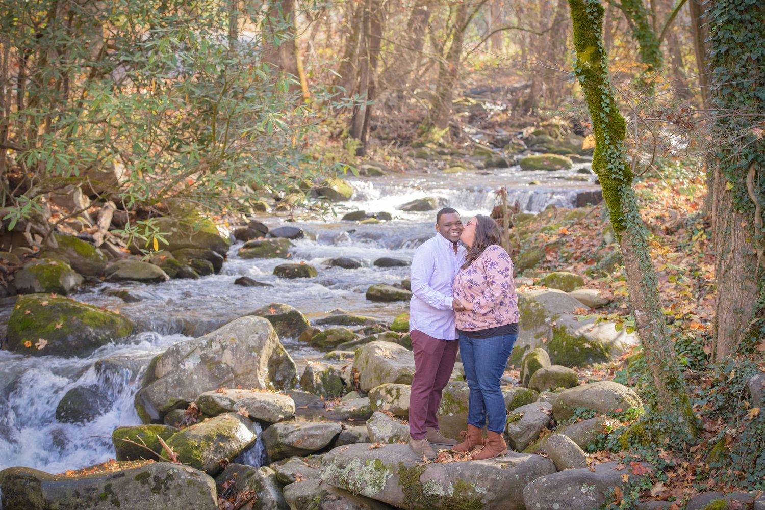 Two people share a tender moment beside a rushing mountain stream surrounded by mossy rocks and autumn forest by Townsend TN Photographer