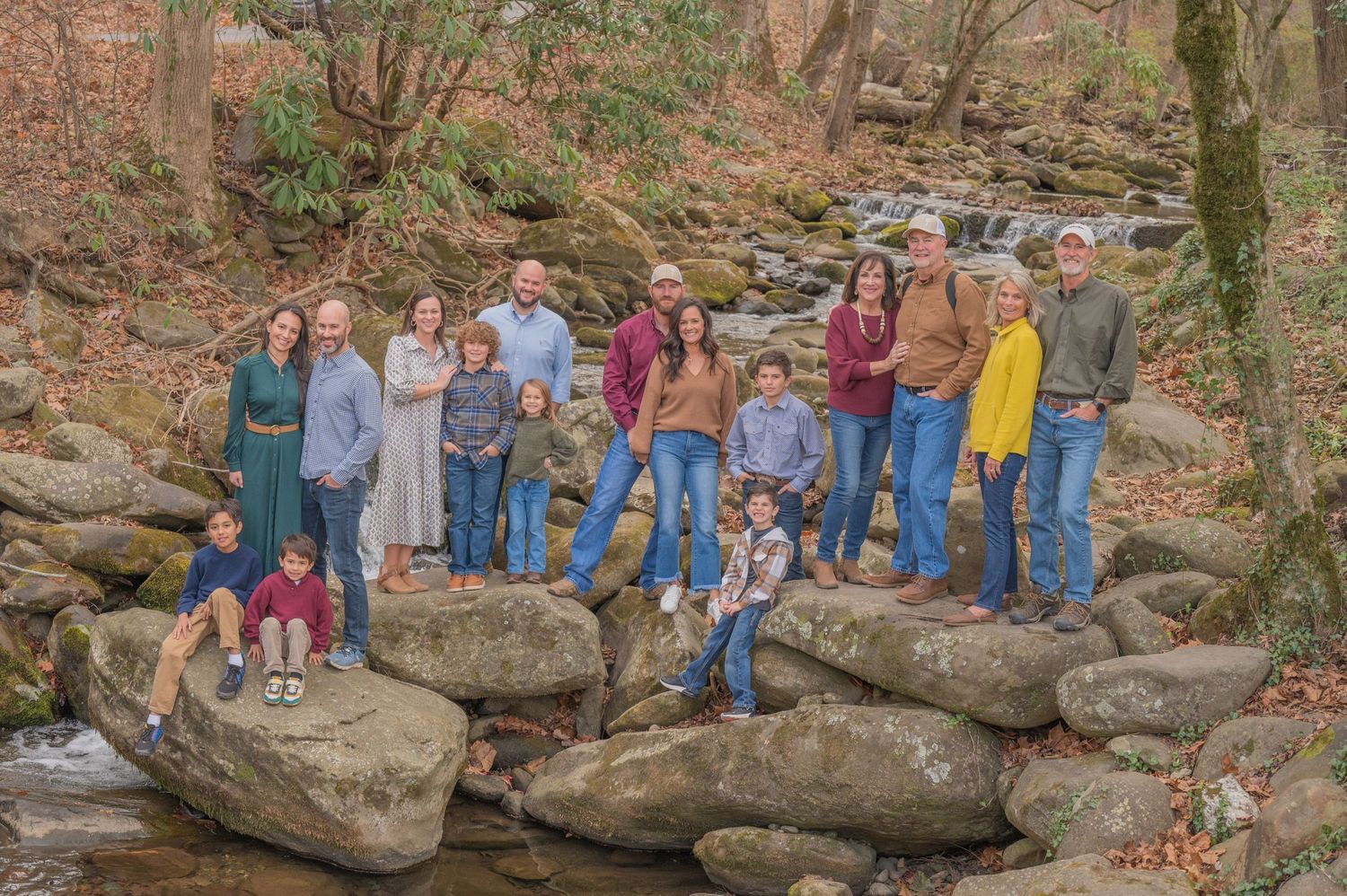 A group stands together on large rocks by a creek in an autumn forest.