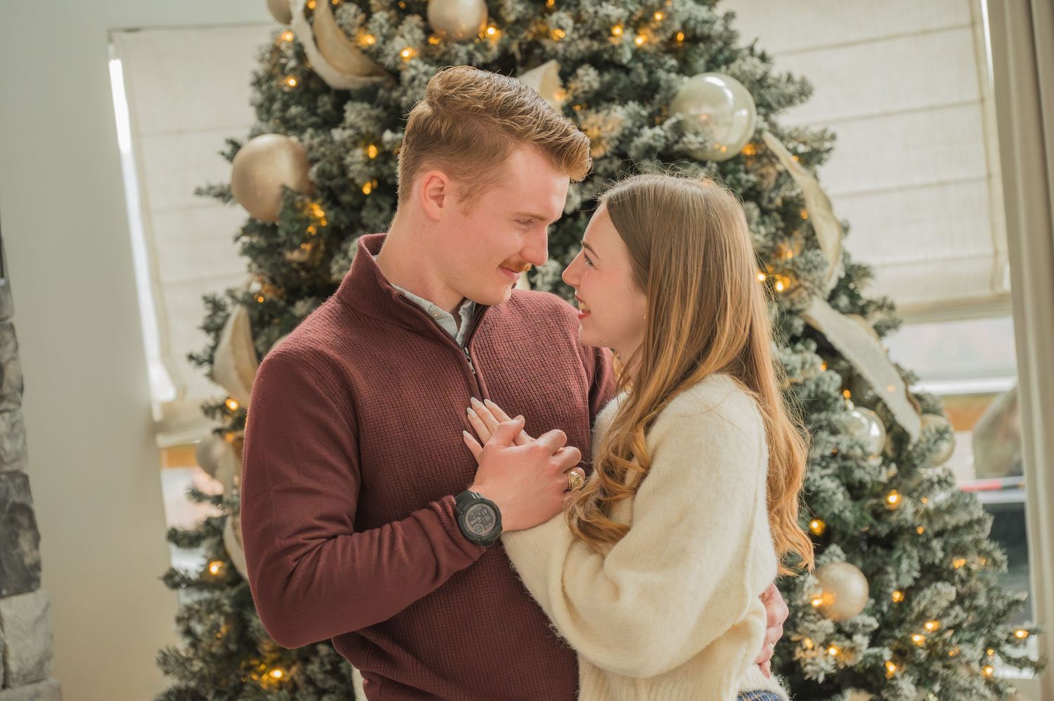 A romantic couple shares an intimate moment in front of a decorated Christmas tree glowing with warm lights by Pigeon Forge Photographer tn.