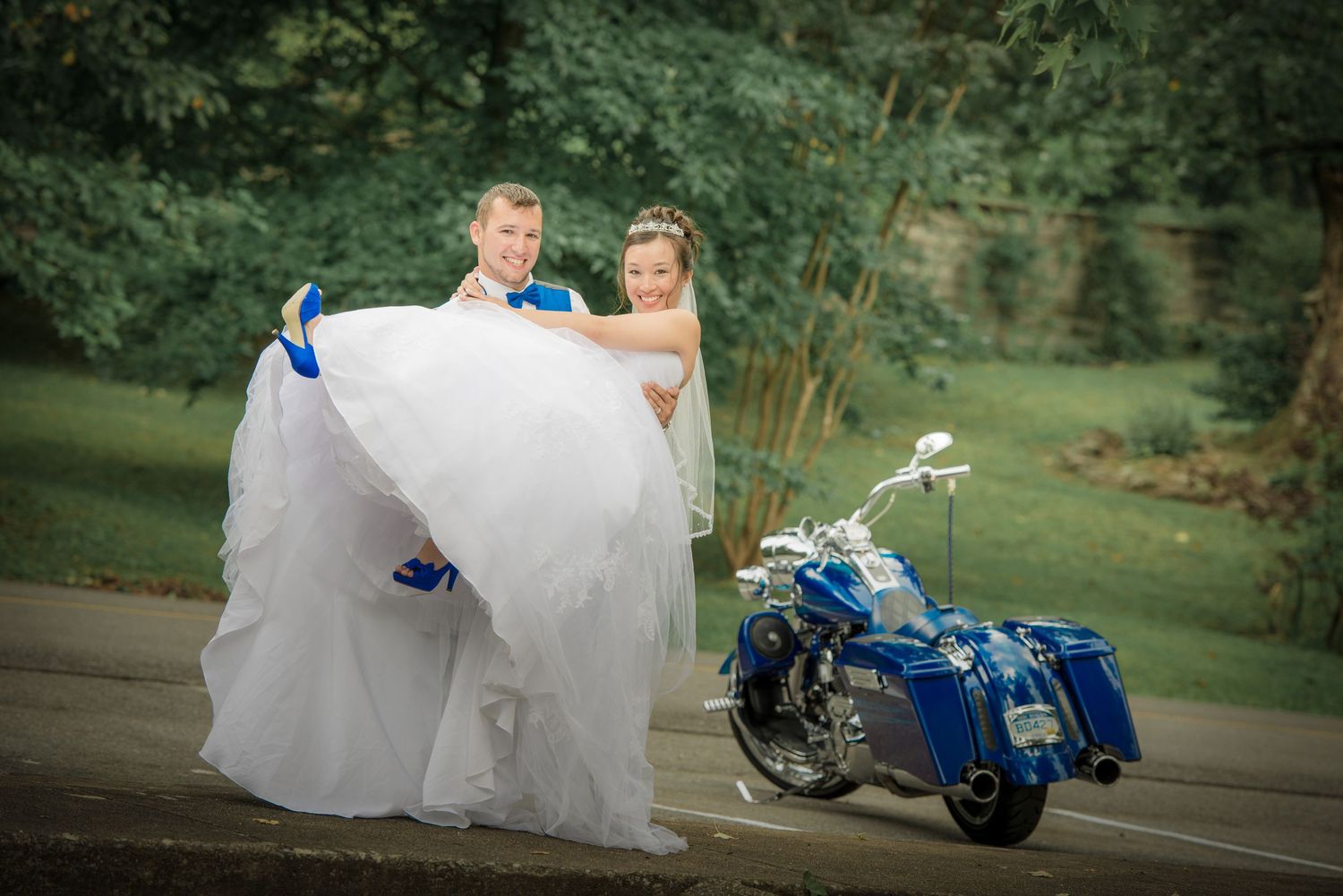 A couple in wedding attire poses next to a custom blue motorcycle with matching saddlebags on a country path by Gatlinburg TN Weddings.