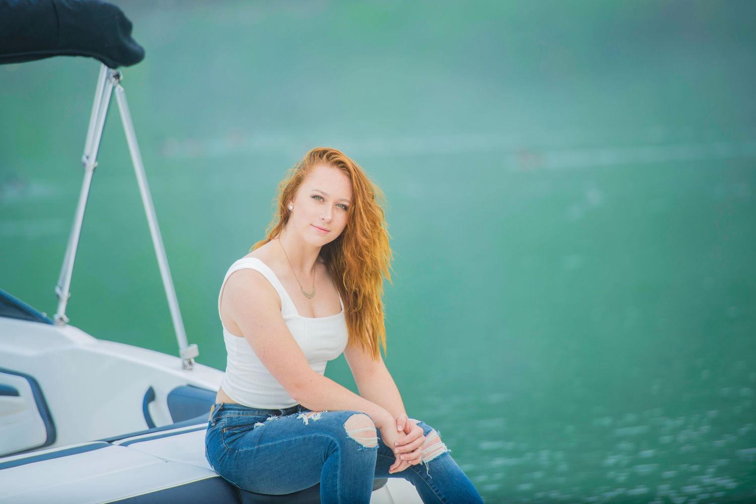 Woman with long red hair sits casually on a boat deck while enjoying a peaceful day on turquoise waters.