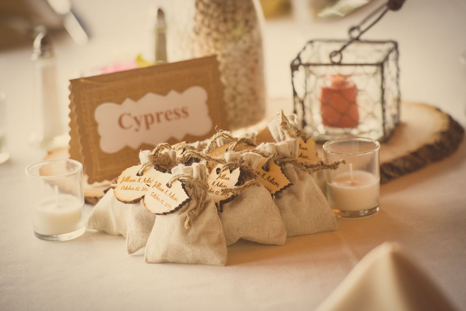 Rustic wedding favors and place cards displayed with candles and decorative elements on a cream tablecloth by Sevierville Photographers.