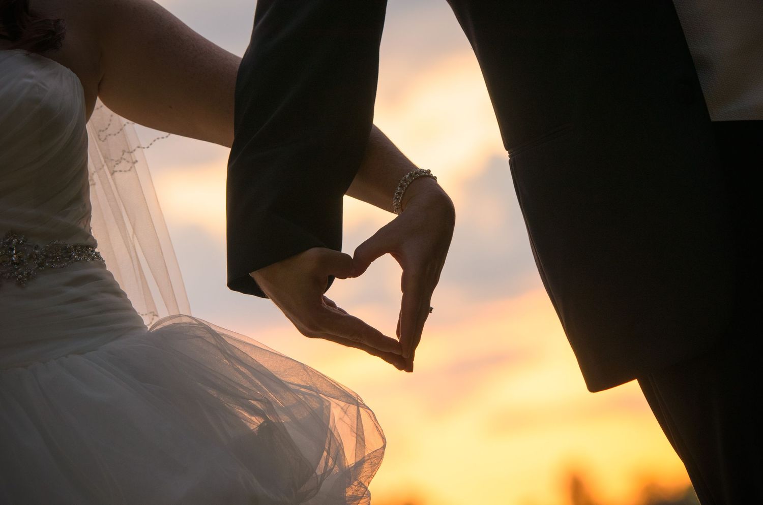 Two silhouetted figures form a heart shape with their hands against a warm sunset sky in Sevierville TN.