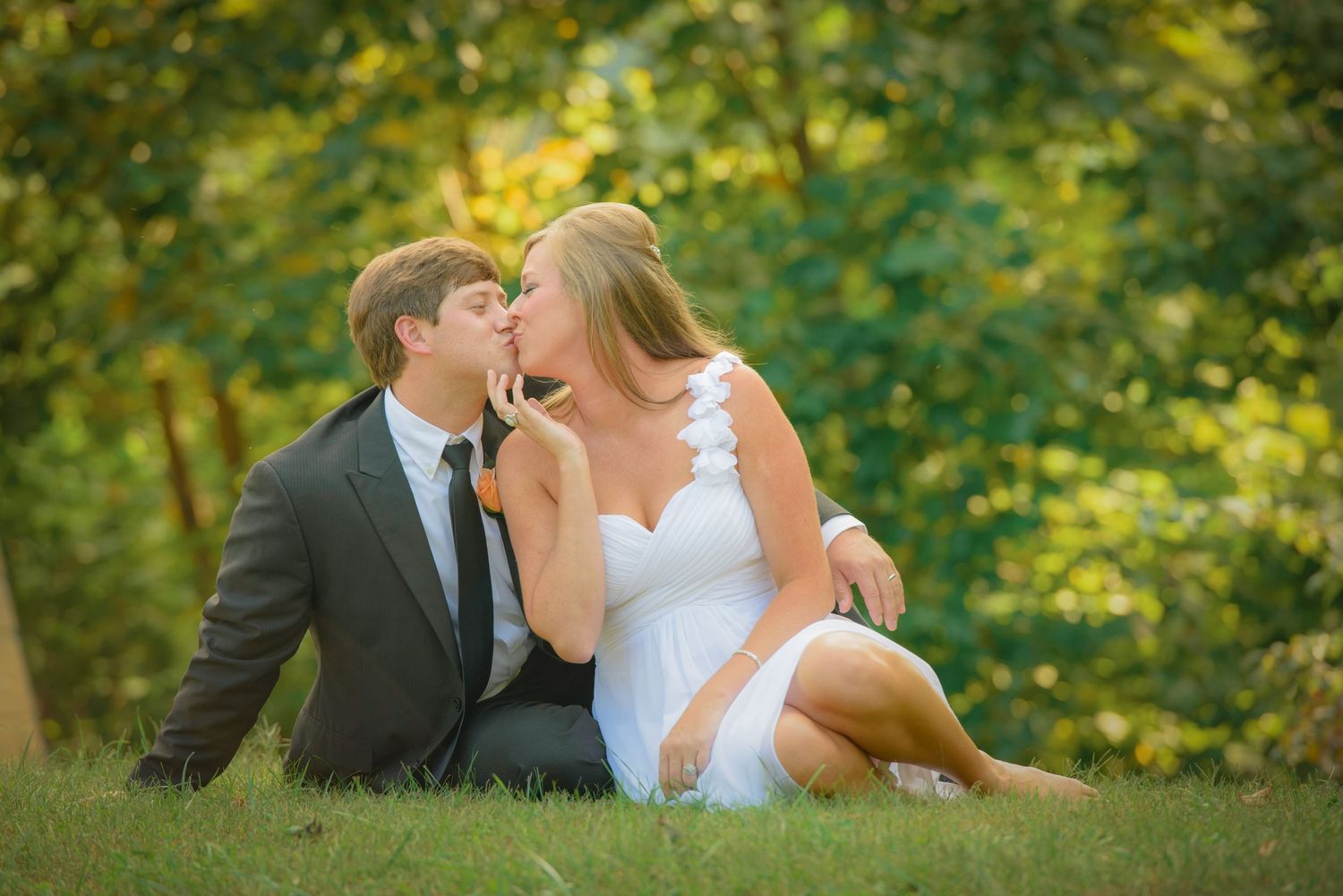 A romantic outdoor portrait of a couple in wedding attire sitting on grass with golden sunlit foliage in background in Sevierville.