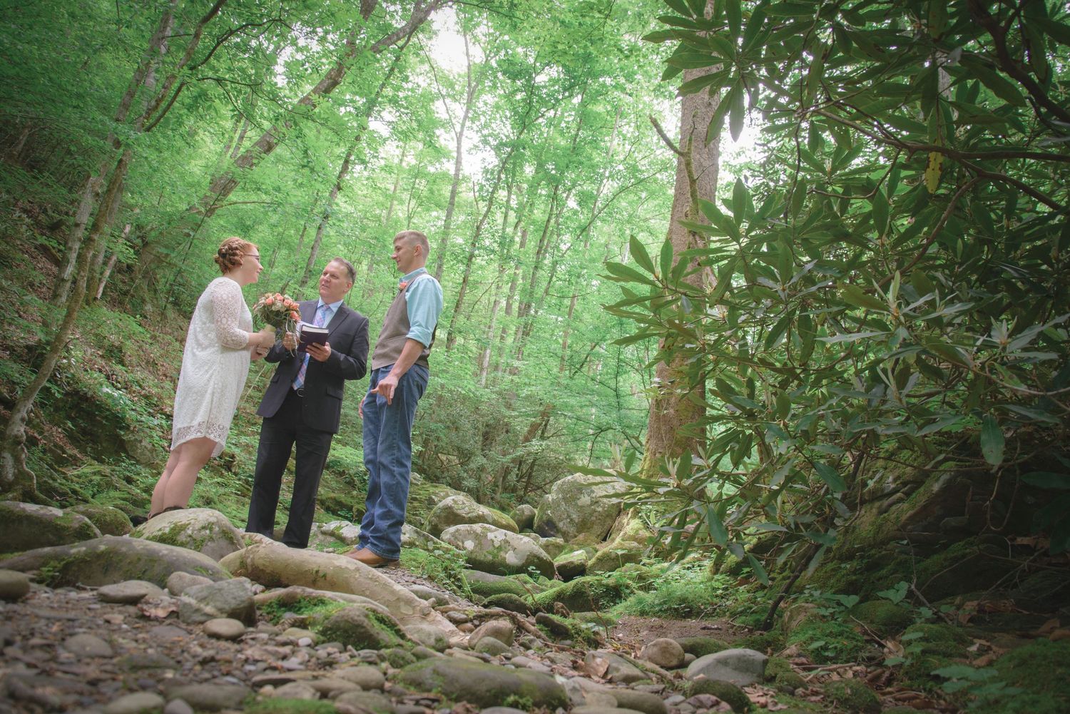 Intimate outdoor ceremony takes place on rocky forest path surrounded by lush green trees and mountain laurel in Pigeon Forge.