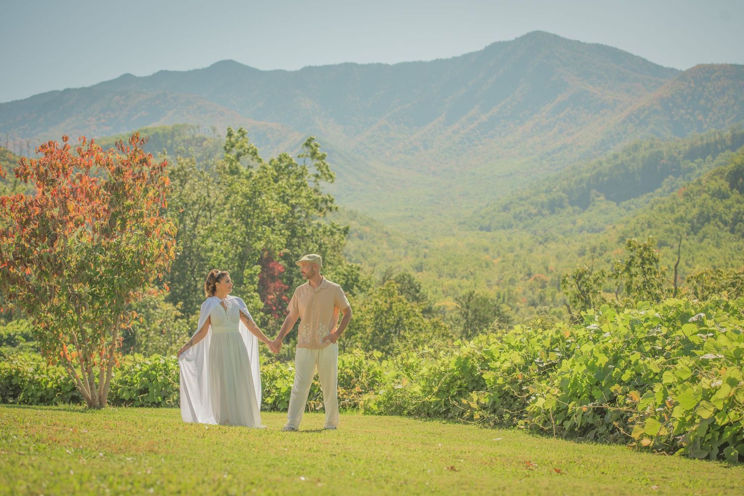 An anniversary couple people stand together overlooking a scenic mountain vista with fall foliage in the Great Smoky Mountains.