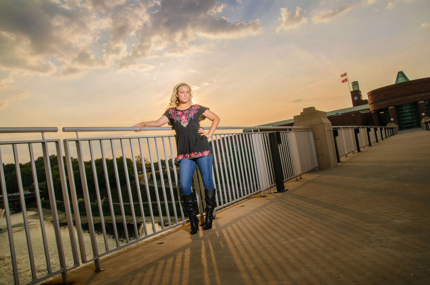 Person stands on wooden boardwalk railing against golden sunset sky over waterfront.