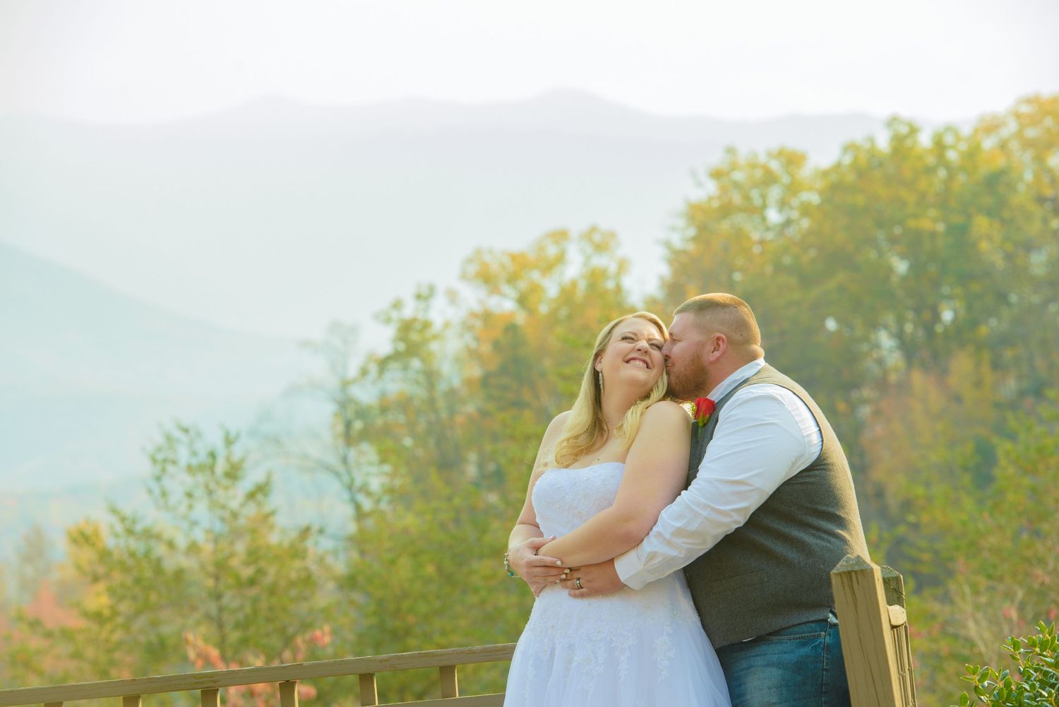A couple embraces on a deck with autumn foliage and mountains in the background during a wedding celebration in Pigeon Forge.
