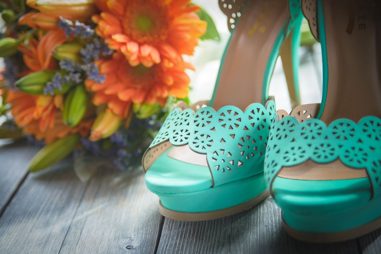 Pigeon Forge Wedding Photographers portrait of Teal laser-cut peep-toe platform heels sit beside orange sunflowers on a dark wooden surface.