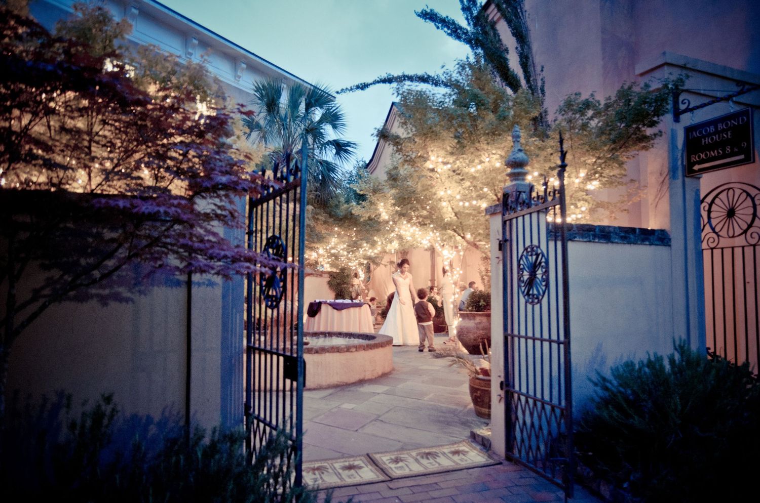 Illuminated wrought iron gates open to an enchanted garden courtyard with twinkling lights and glowing decorations in Sevierville TN.