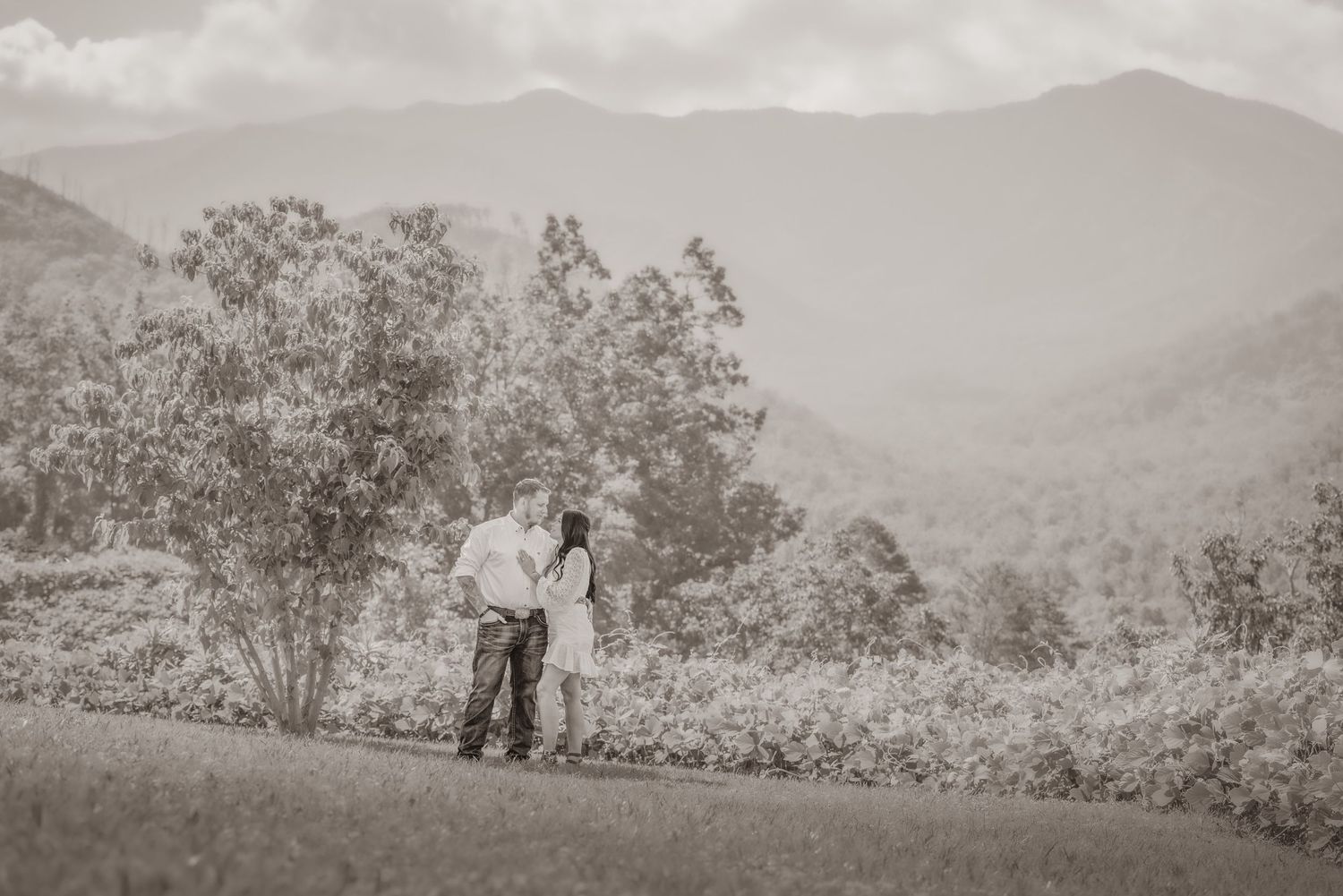 An engagement shares a romantic moment on a hilltop overlooking mountain ranges in black and white photography by Gatlinburg Photographers.