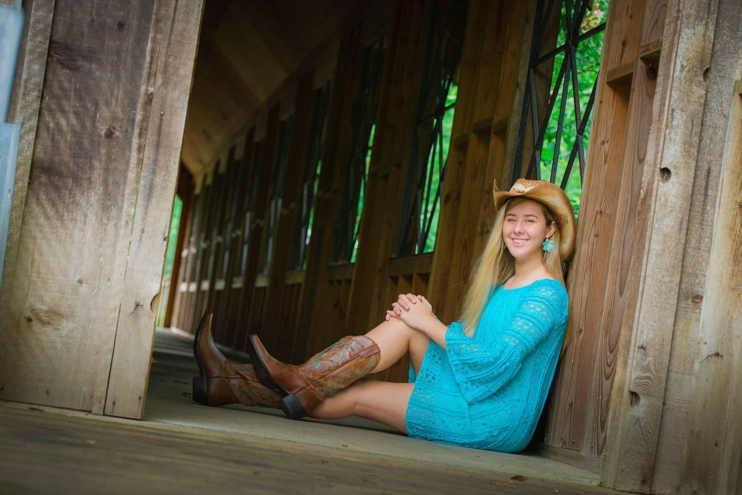 Person in turquoise dress sitting on wooden bridge deck with bright green backlighting and rustic ambiance.