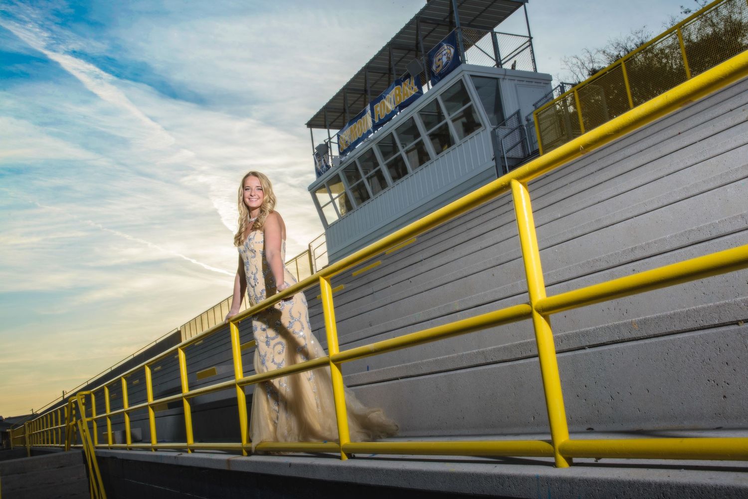 A person stands on yellow railing at sunset with a control tower in the background at a racing track.