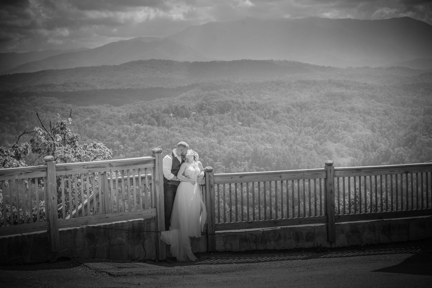 A couple shares a romantic moment on a mountain overlook deck with scenic rolling hills in the background in by Pigeon Forge TN.