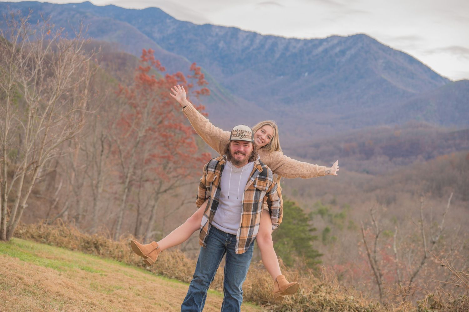 Couple enjoying a playful moment on a scenic hillside with mountains and bare winter trees in the background by Sevierville TN Photographers