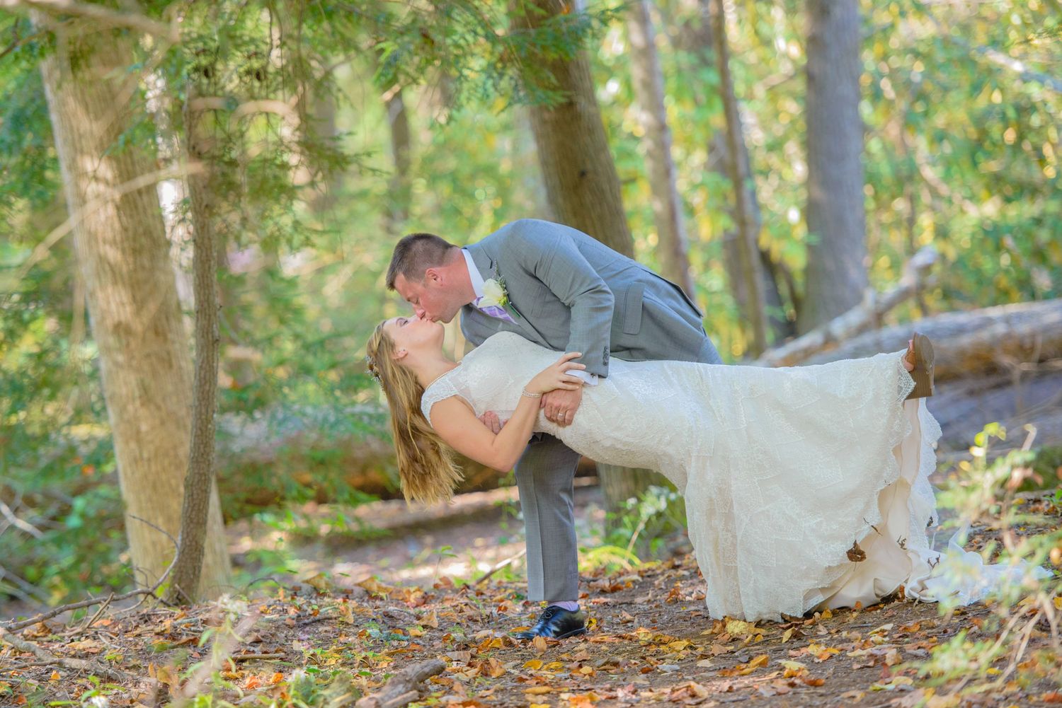 A romantic outdoor woodland wedding portrait shows a graceful dip pose amongst fallen autumn leaves by Pigeon Forge Wedding Photographers.
