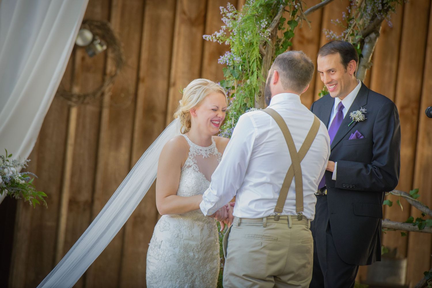 A joyful moment during a rustic barn wedding ceremony with wood paneling and flowing white curtains in the background in wears valley TN.