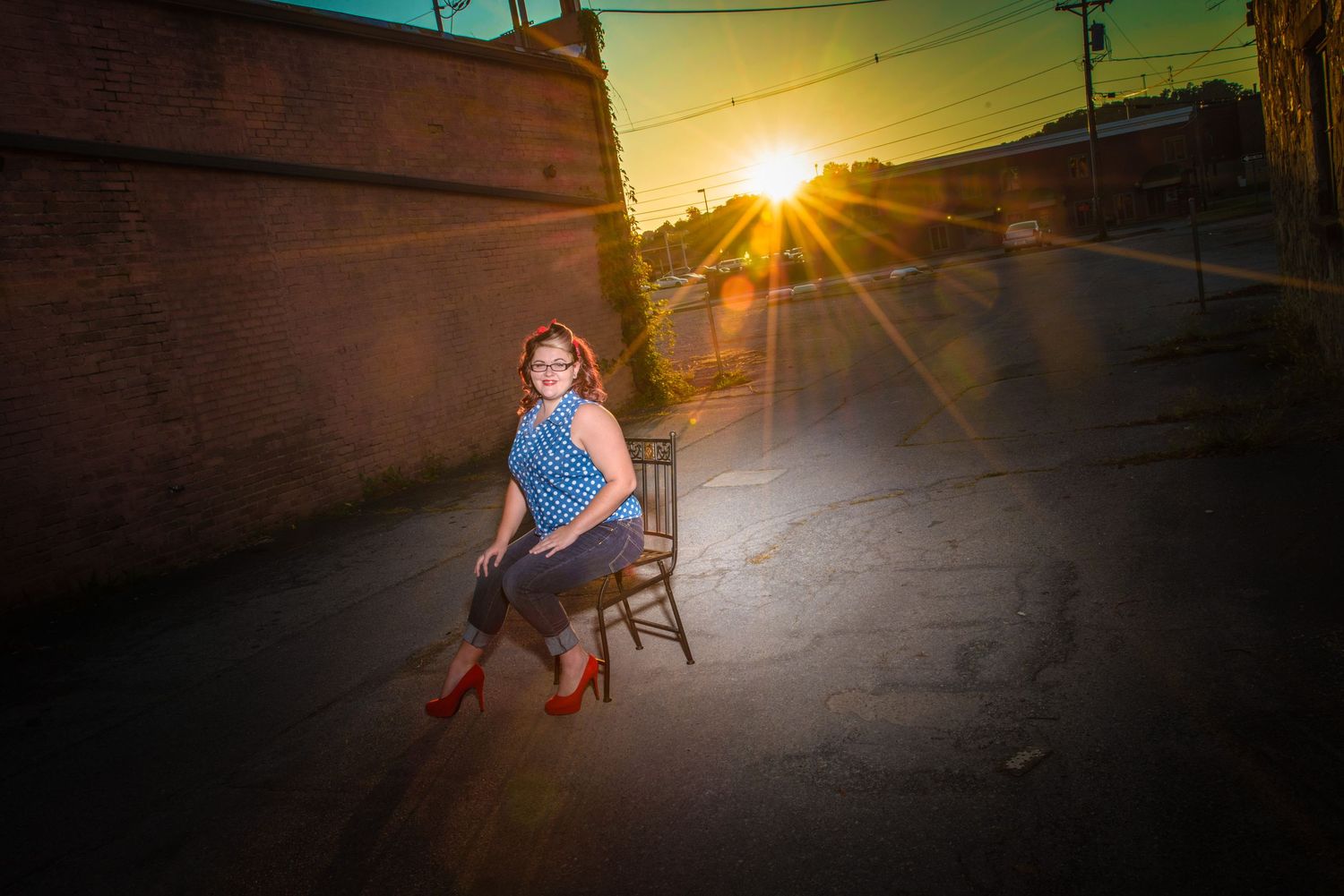 A person sits on a vintage wooden chair on a street as golden sunset sunbeams shine through buildings in the background.