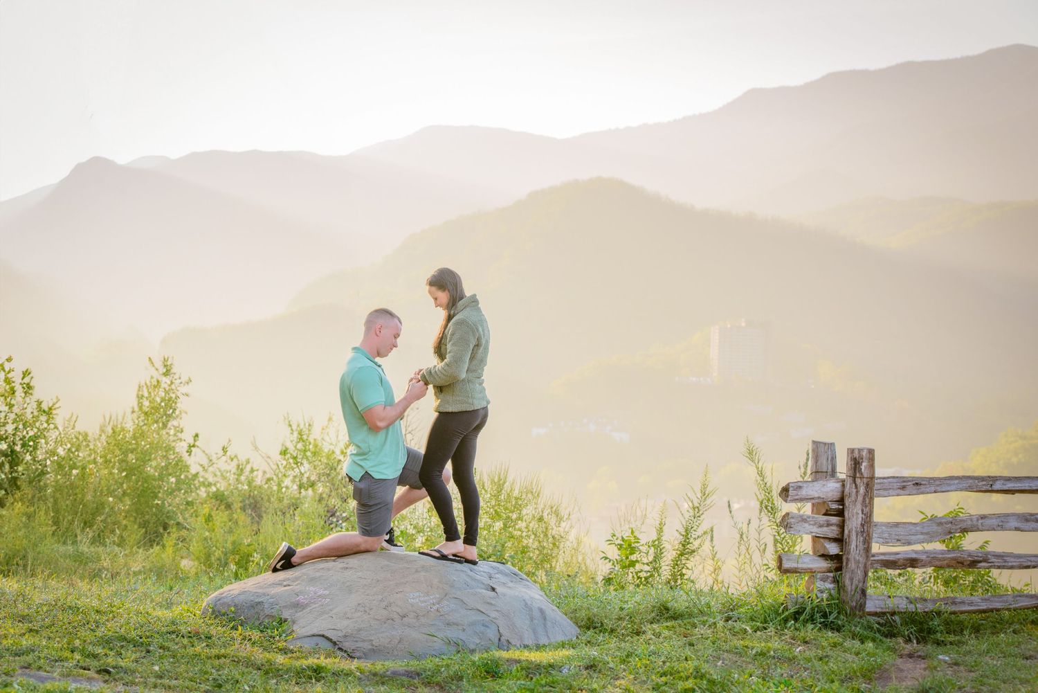 A surprise proposal large rock during sunset in the misty mountains with a rustic fence nearby by Gatlinburg TN Photographers.