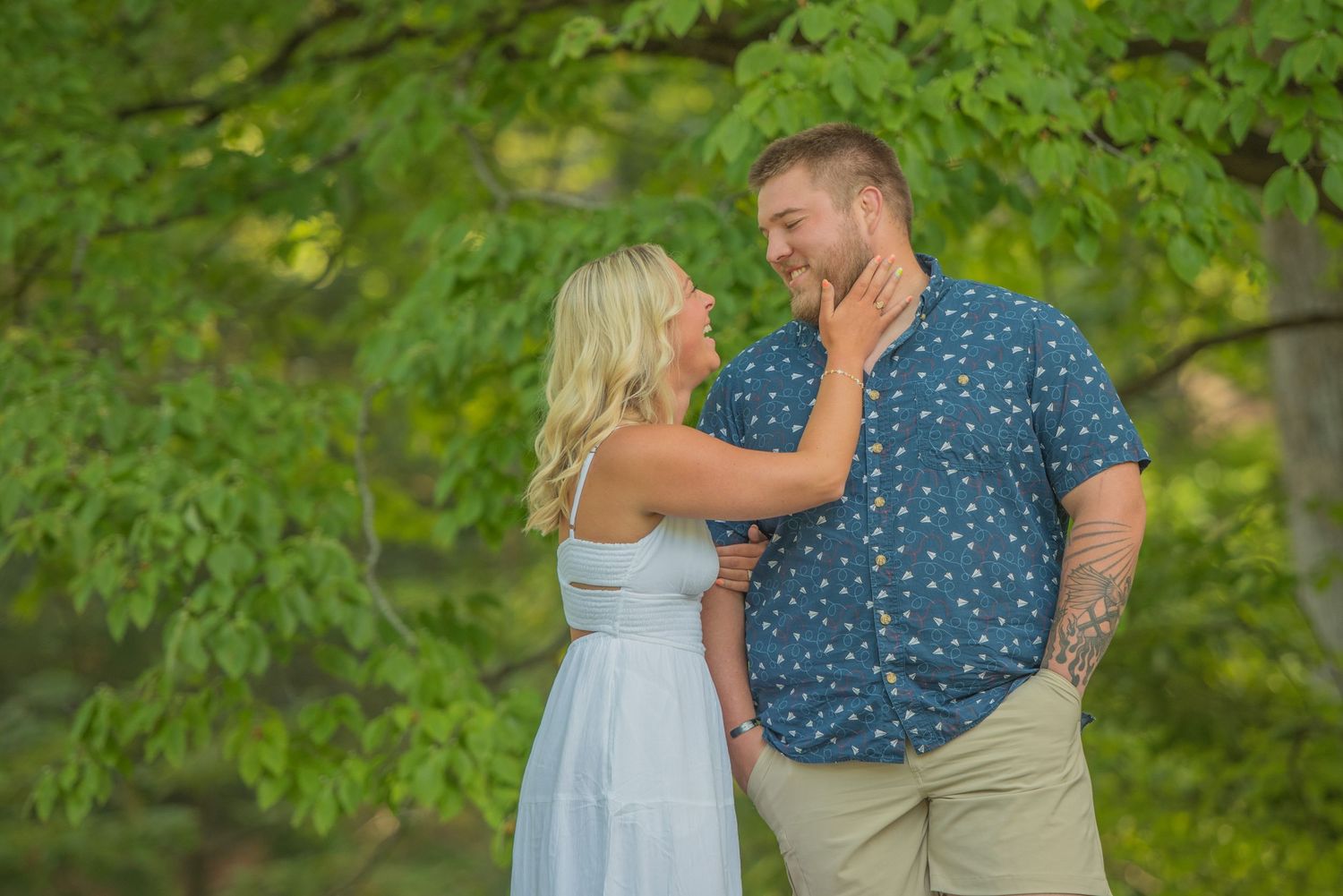 A romantic outdoor couple sharing an intimate moment under lush green trees during a summer photo session by Sevierville TN Photographers.