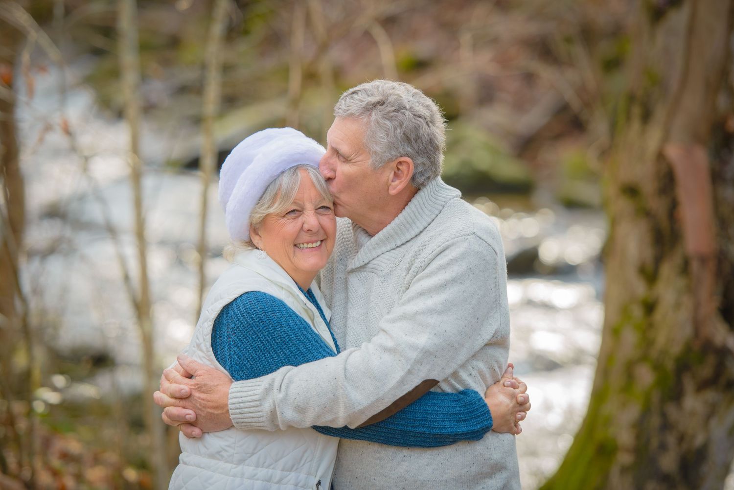 An elderly couple embraces and shares a tender moment outdoors near a flowing stream by Gatlinburg TN Photographers.