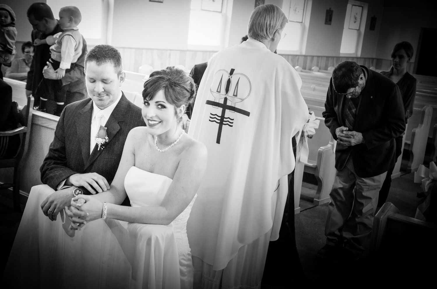 Black and white photo of a religious wedding ceremony with a priest wearing white robes with a cross emblem in Sevierville TN.