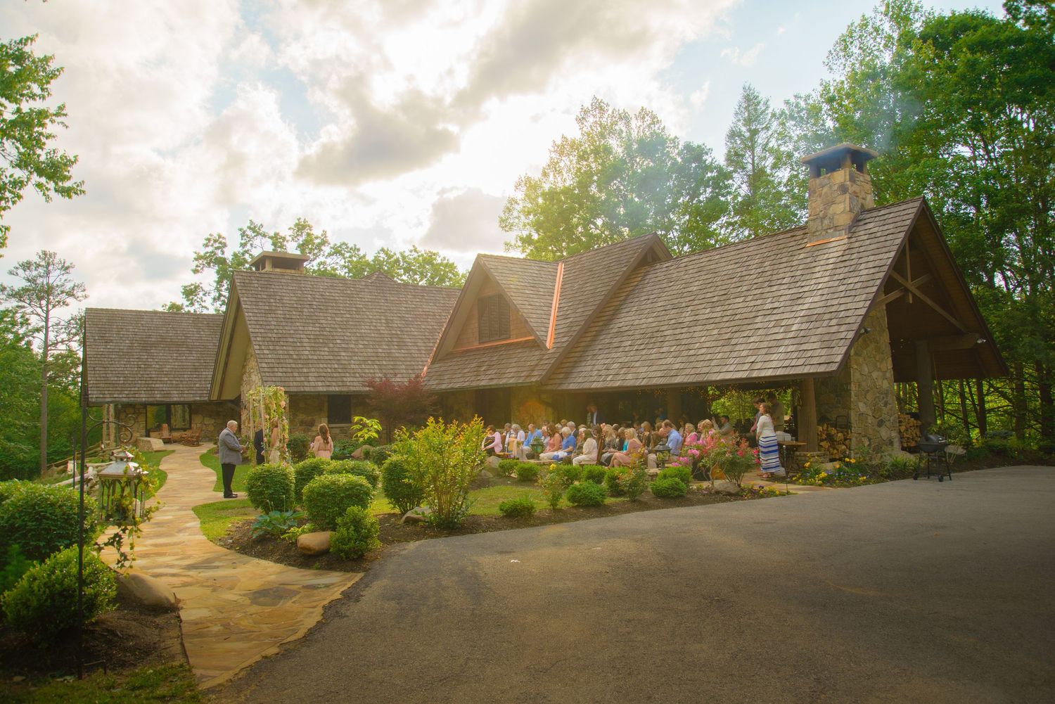 Rustic stone cottage with multiple dormers and colorful garden landscaping along curving driveway at sunset by Gatlinburg TN Weddings.