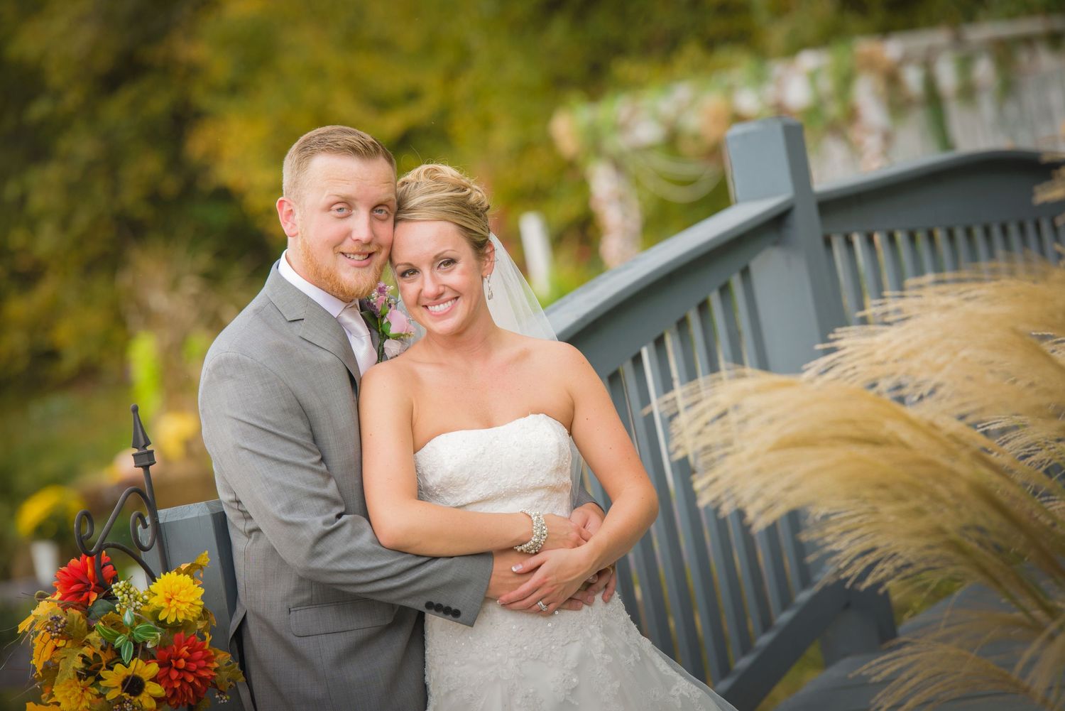 Newlywed couple embraces on a bridge with autumn foliage and colorful floral bouquet in the background by Gatlinburg Wedding Photographers.