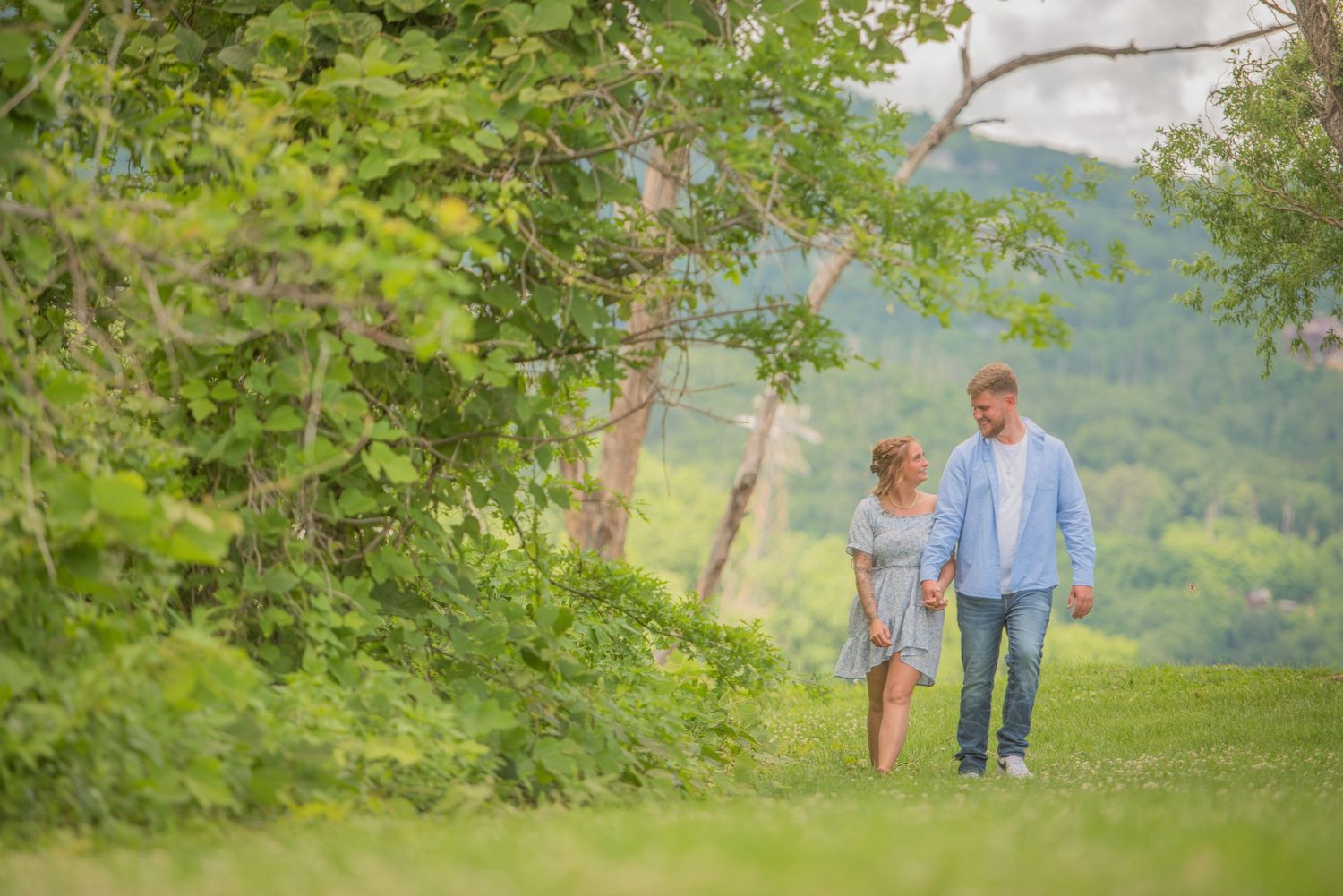 Two people holding hands while walking together on a grassy path surrounded by lush greenery and mountains by Gatlinburg Townsend TN.