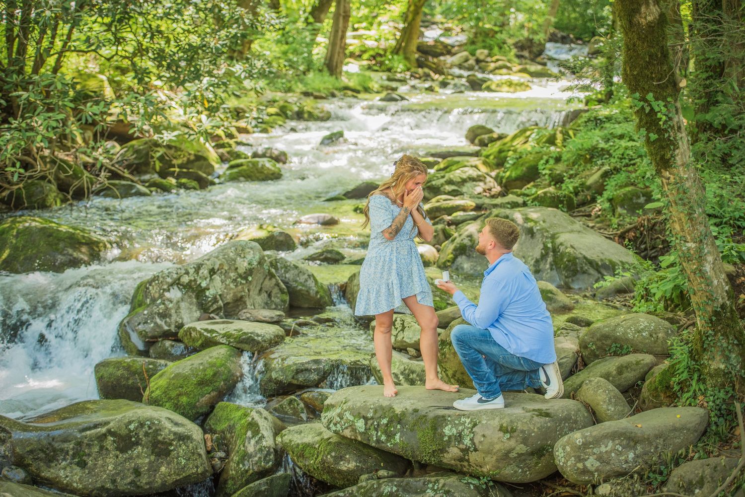 A scenic proposal moment unfolds on moss-covered rocks beside a cascading mountain stream in a lush forest setting in gatlinburg tn.