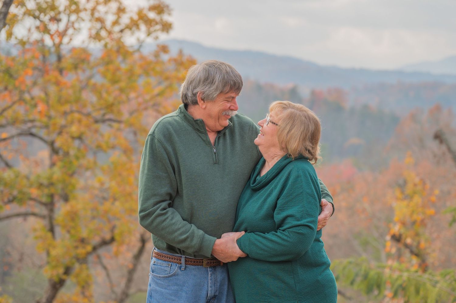 An affectionate couple embraces while enjoying autumn mountain views with fall foliage in the background by Sevierville TN Photographers.