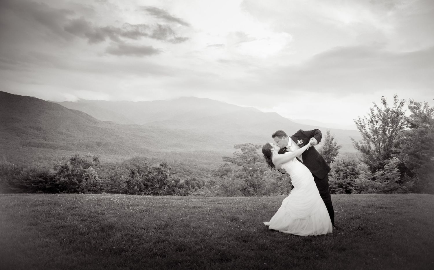 A romantic black and white wedding photograph of a couple dancing on a hilltop overlooking a misty mountain landscape in Gatlinburg TN.