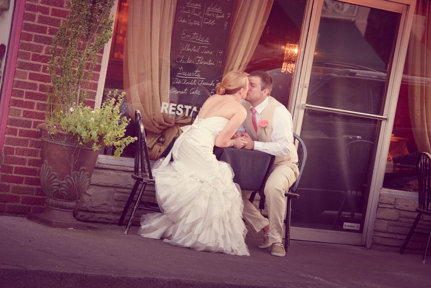 A romantic wedding photo shows a couple sharing an intimate moment on a bench outside a brick storefront in Downtown Sevierville TN.