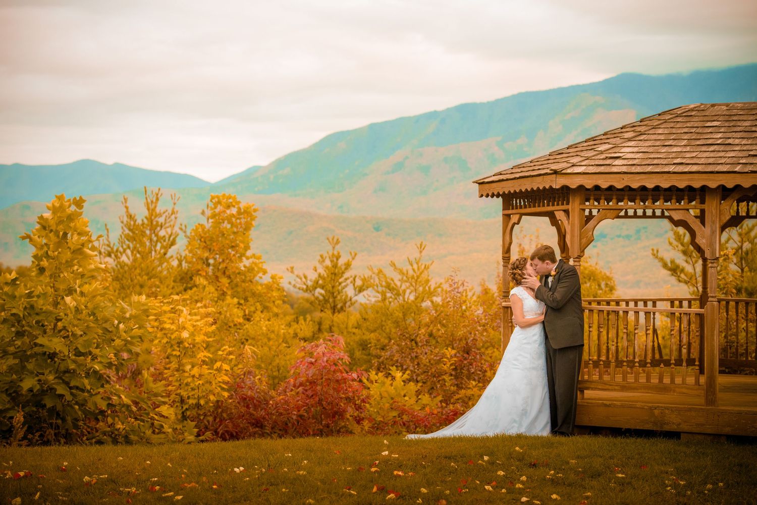 A couple shares a romantic moment at a wooden gazebo surrounded by autumn foliage and mountain views by Gatlinburg Wedding Photographers.