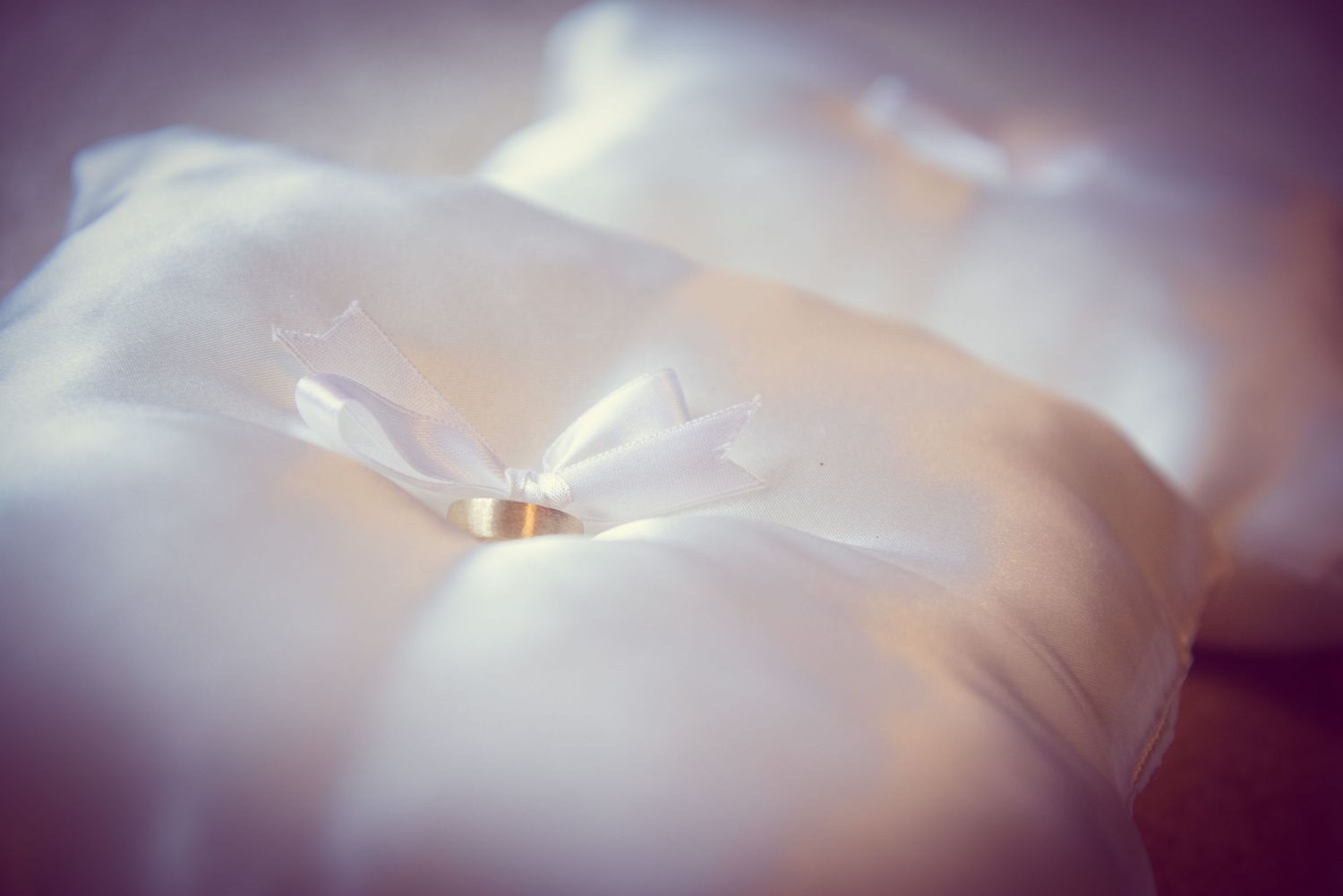 Golden wedding rings rest delicately on soft white fabric with dreamy lighting effects in Cosby TN