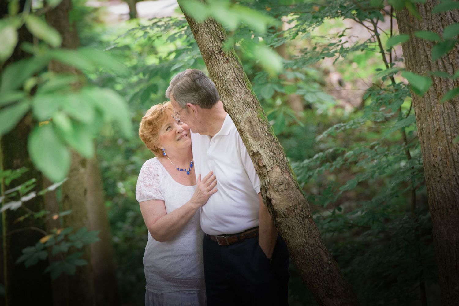 Two people in white shirts share a tender moment among trees and greenery in a natural outdoor setting by Gatlinburg TN Photographers.