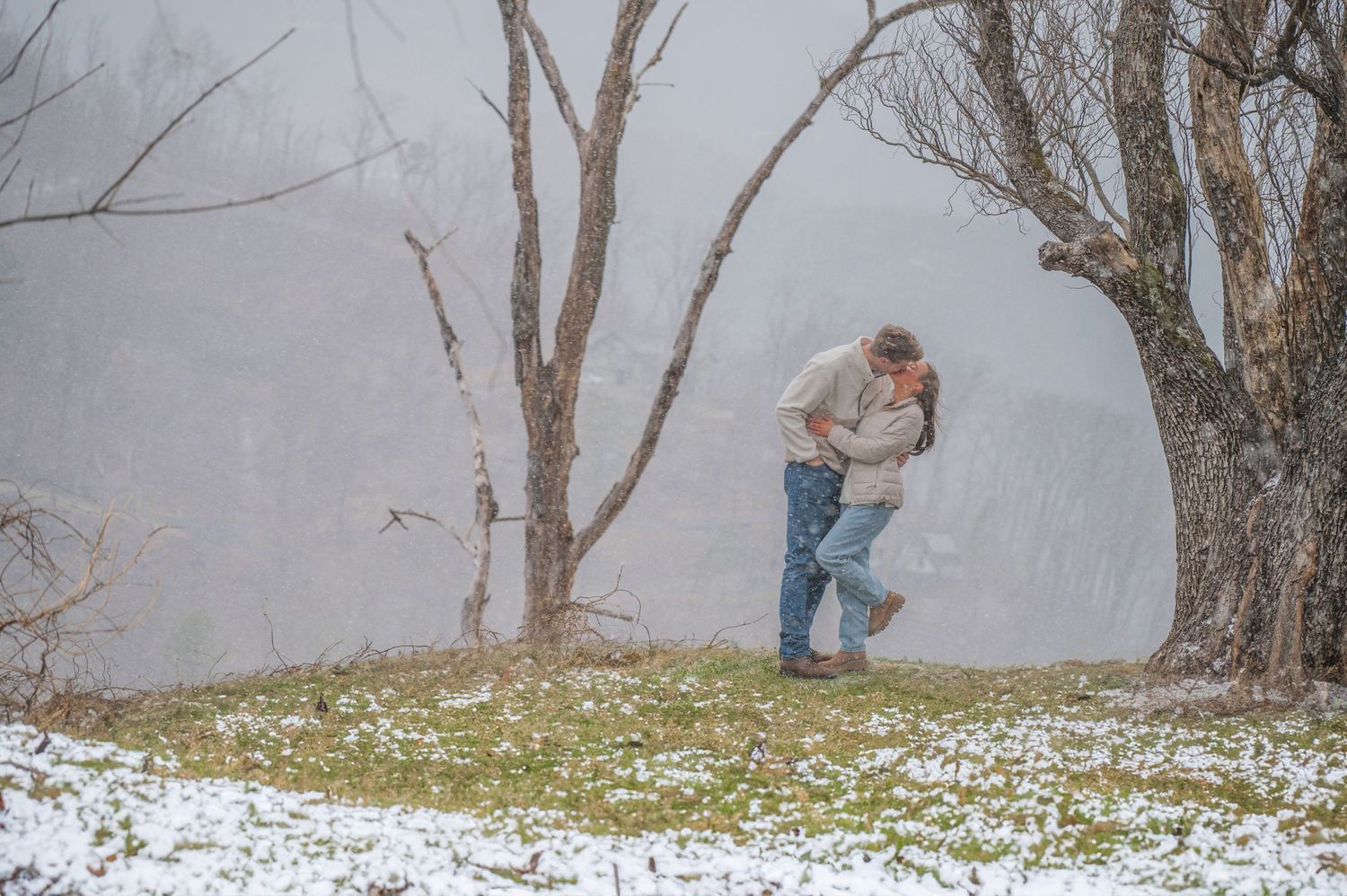 A couple embraces on a snowy hilltop with bare trees in a dreamy winter landscape by Gatlinburg TN Photographers.