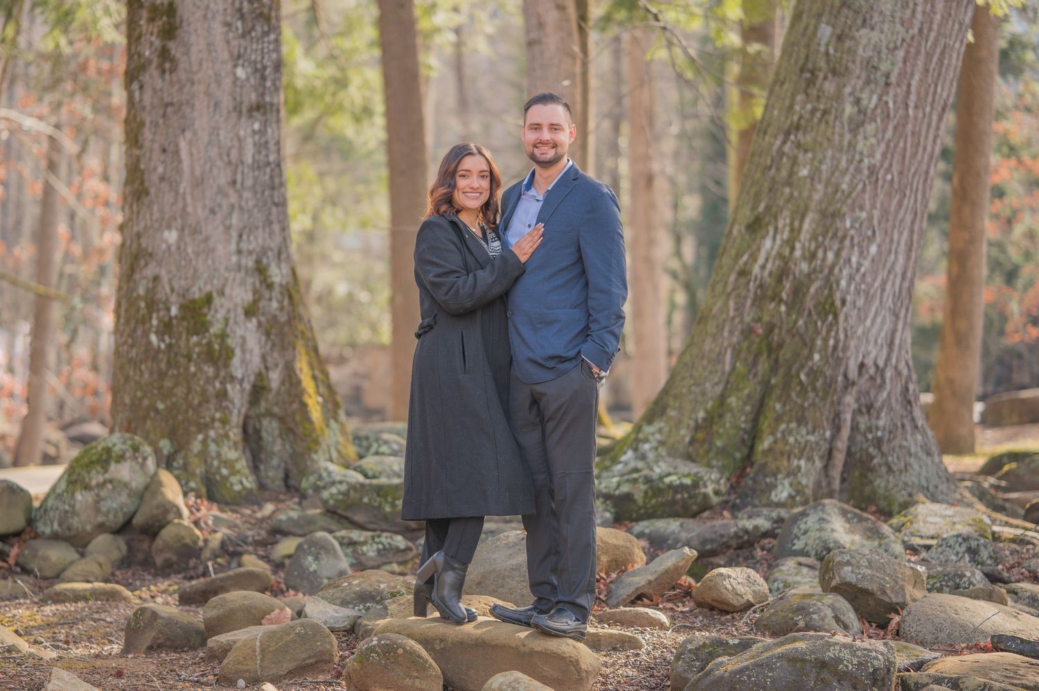 A couple stands between two large trees on a rocky forest path during autumn by Sevierville TN Photographers.