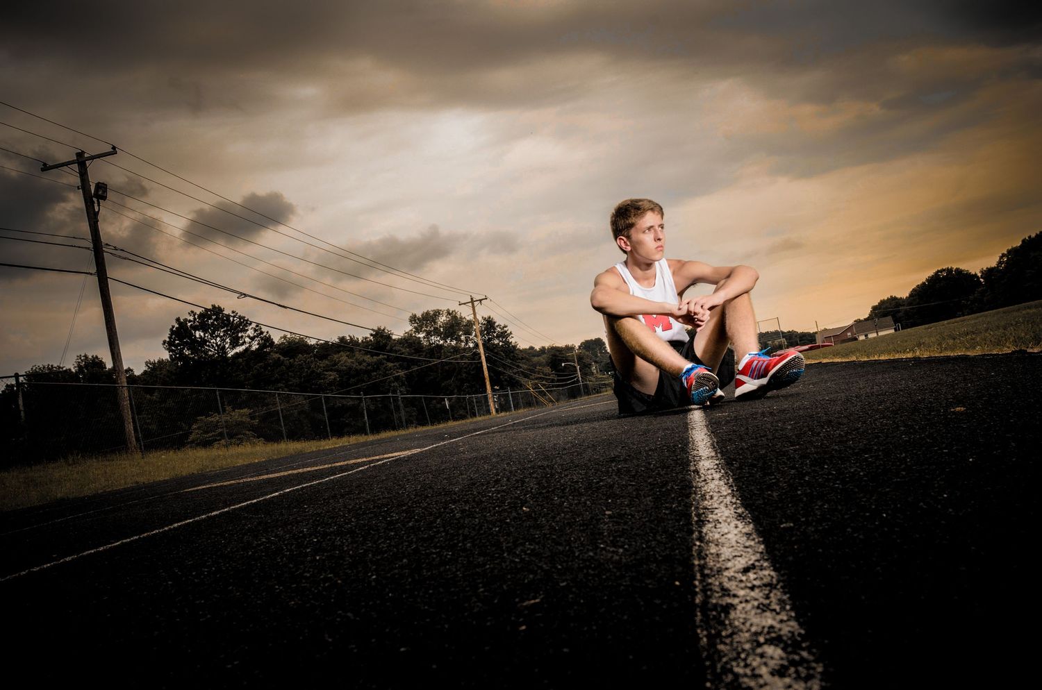 A person sits on a double yellow line of a road at sunset with dramatic cloudy sky overhead.