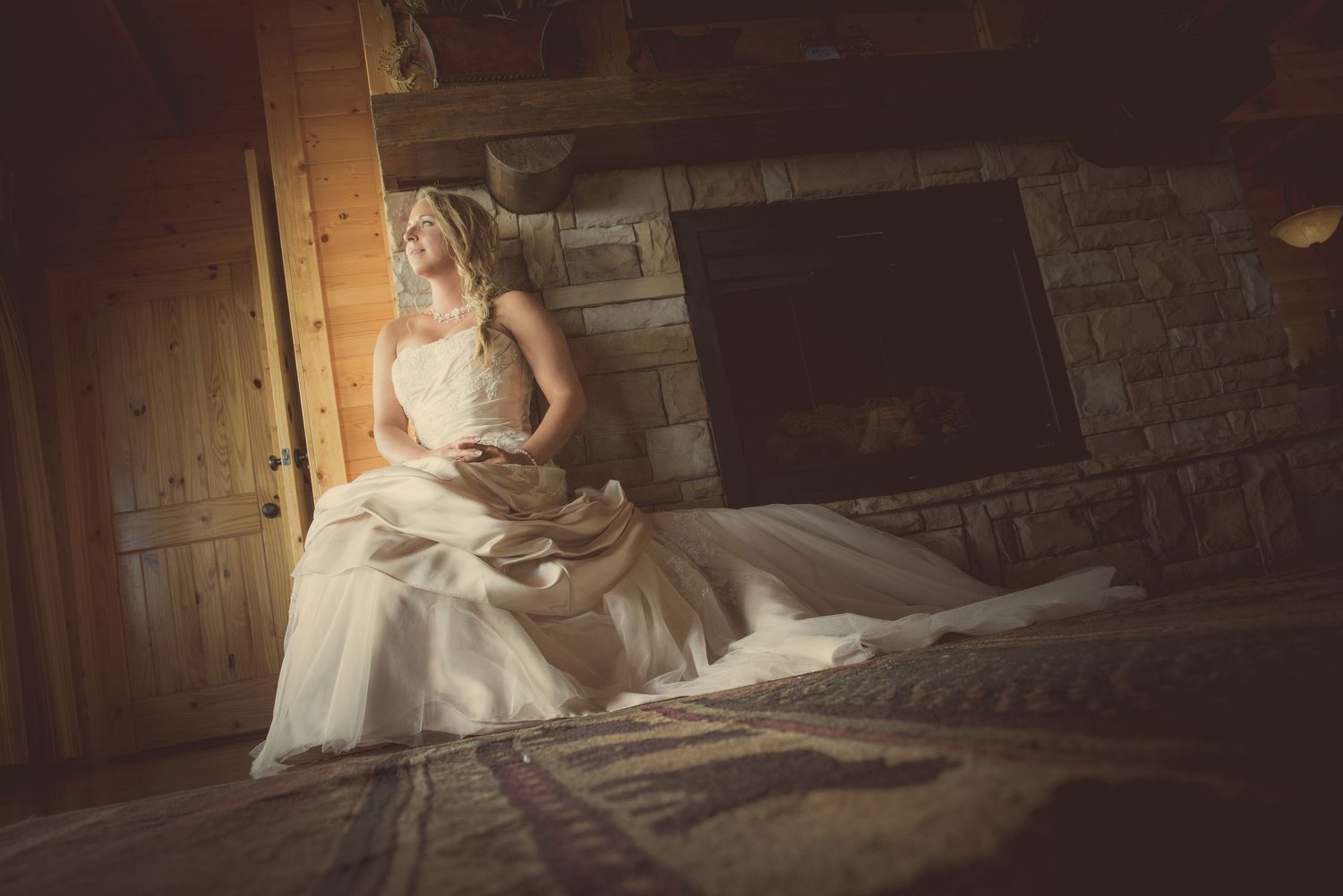 Sevierville Wedding Photographer portrait of bride in an elegant white gown poses in dramatic lighting inside a rustic wooden barn setting.