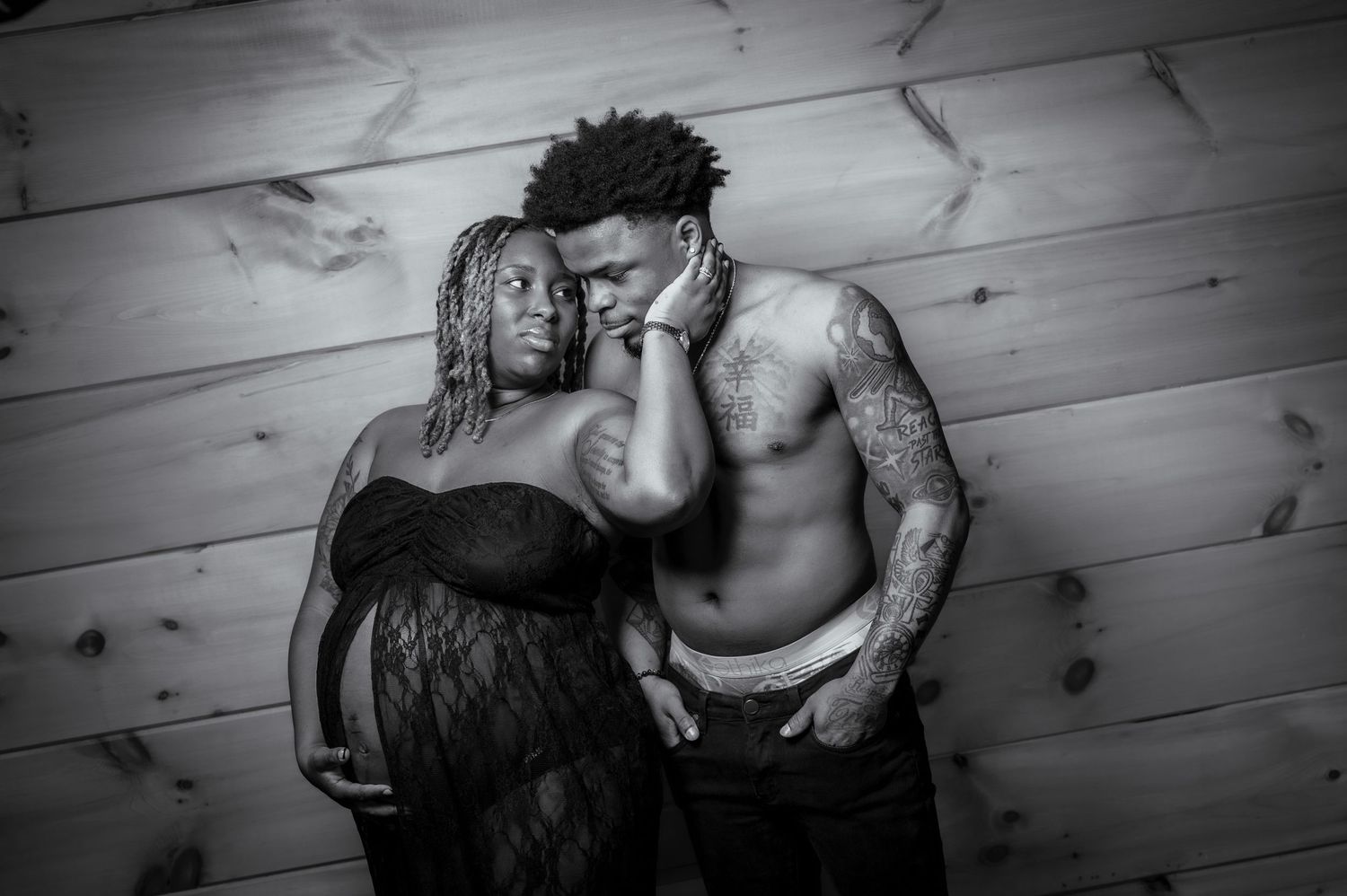 A black and white intimate maternity photo shows an expecting couple in a tender embrace against a wooden wall by Gatlinburg TN Photographer