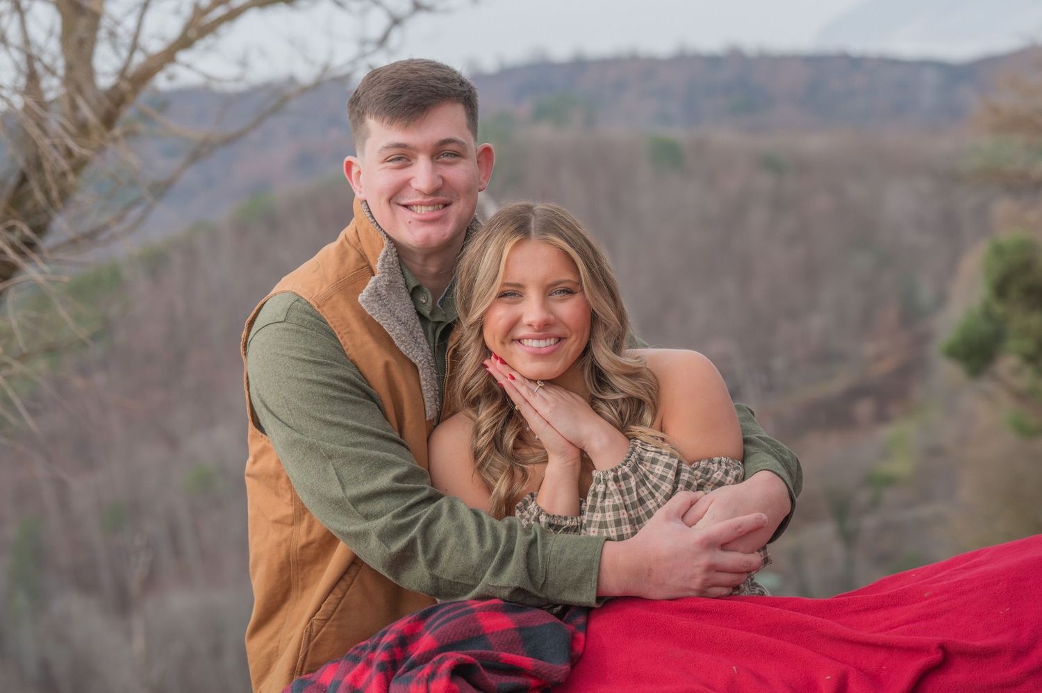A couple enjoys a cozy moment together on a mountain overlook with a red blanket during autumn by Sevierville TN Photographers.