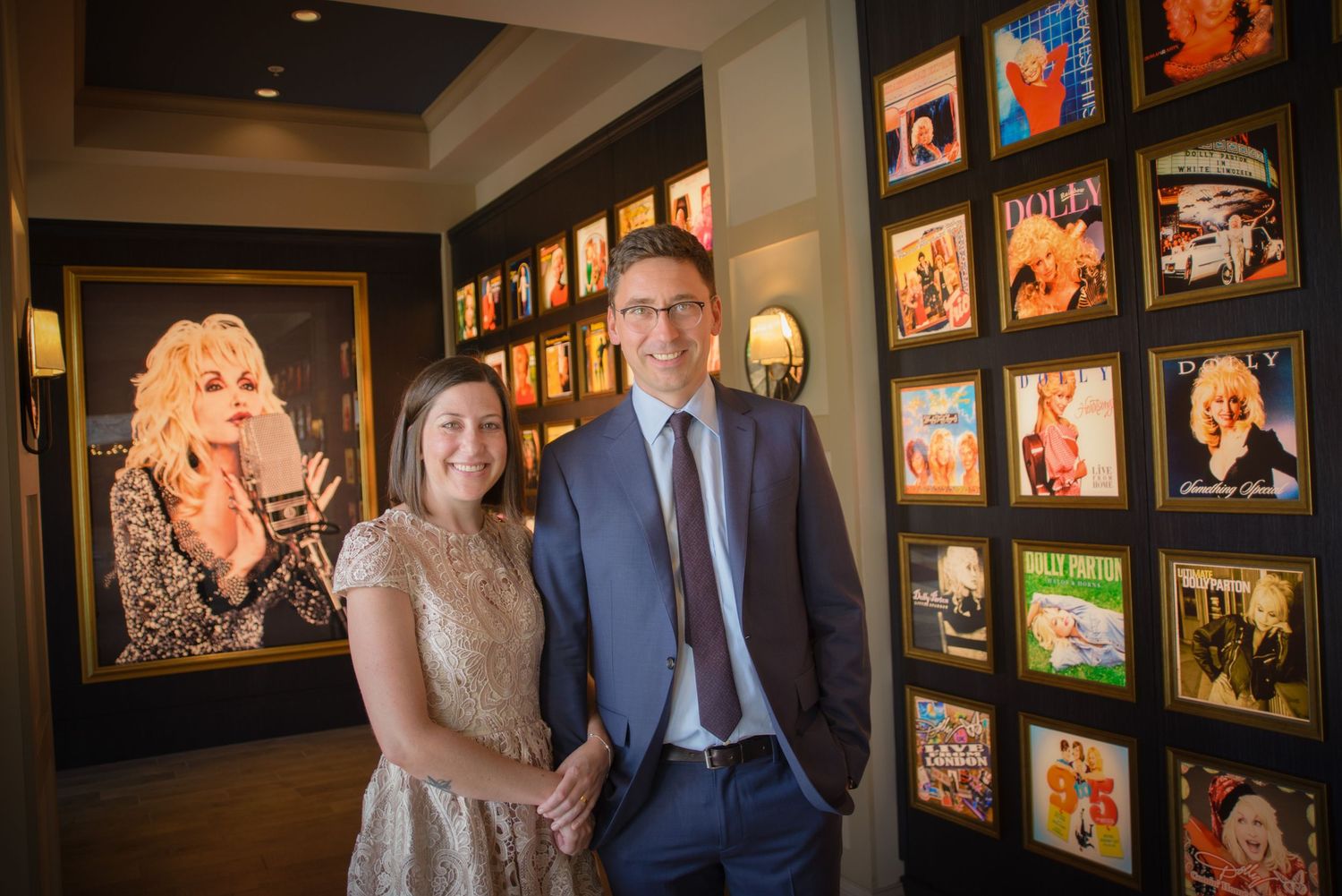 Couple stand in front of a gallery wall featuring colorful framed photographs and  Dolly artwork at Dollywood's DreamMore Resort and Spa.