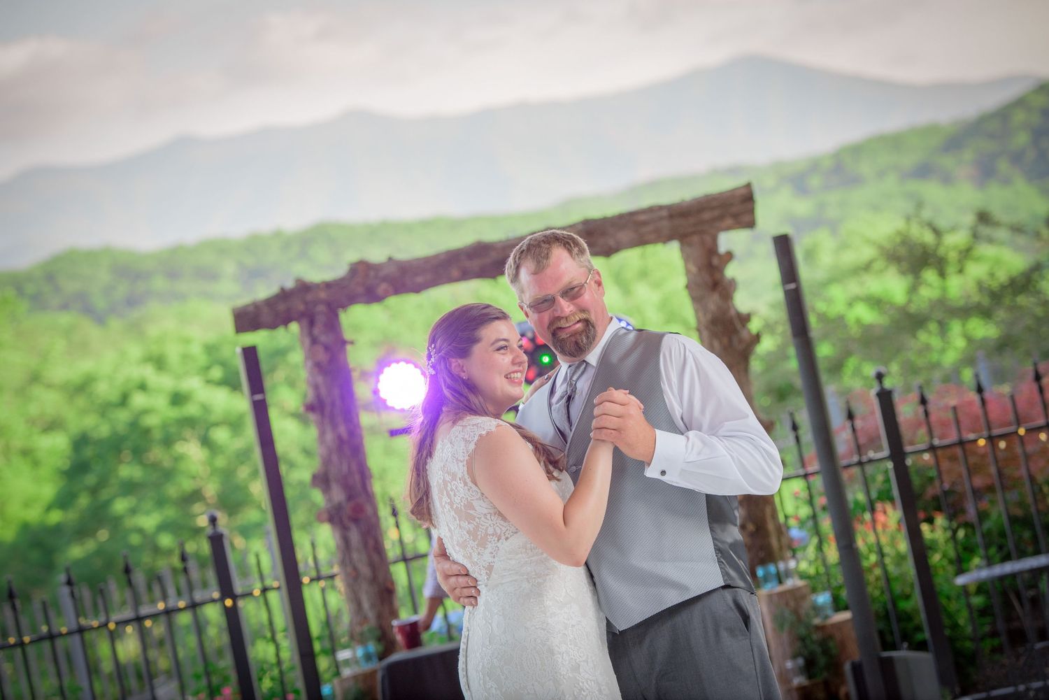 A couple shares their first dance at a scenic mountain wedding venue with purple lighting and lush green background in Pigeon Forge TN.