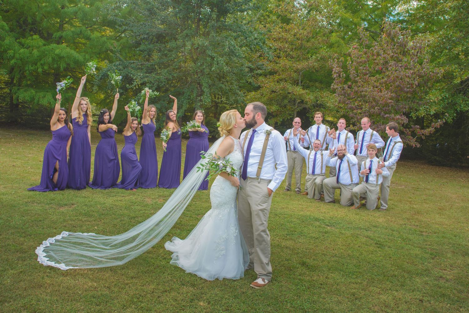 Wedding party wearing purple dresses and blue ties pose on a green lawn during outdoor celebration by Pigeon Forge Wedding Photographers.
