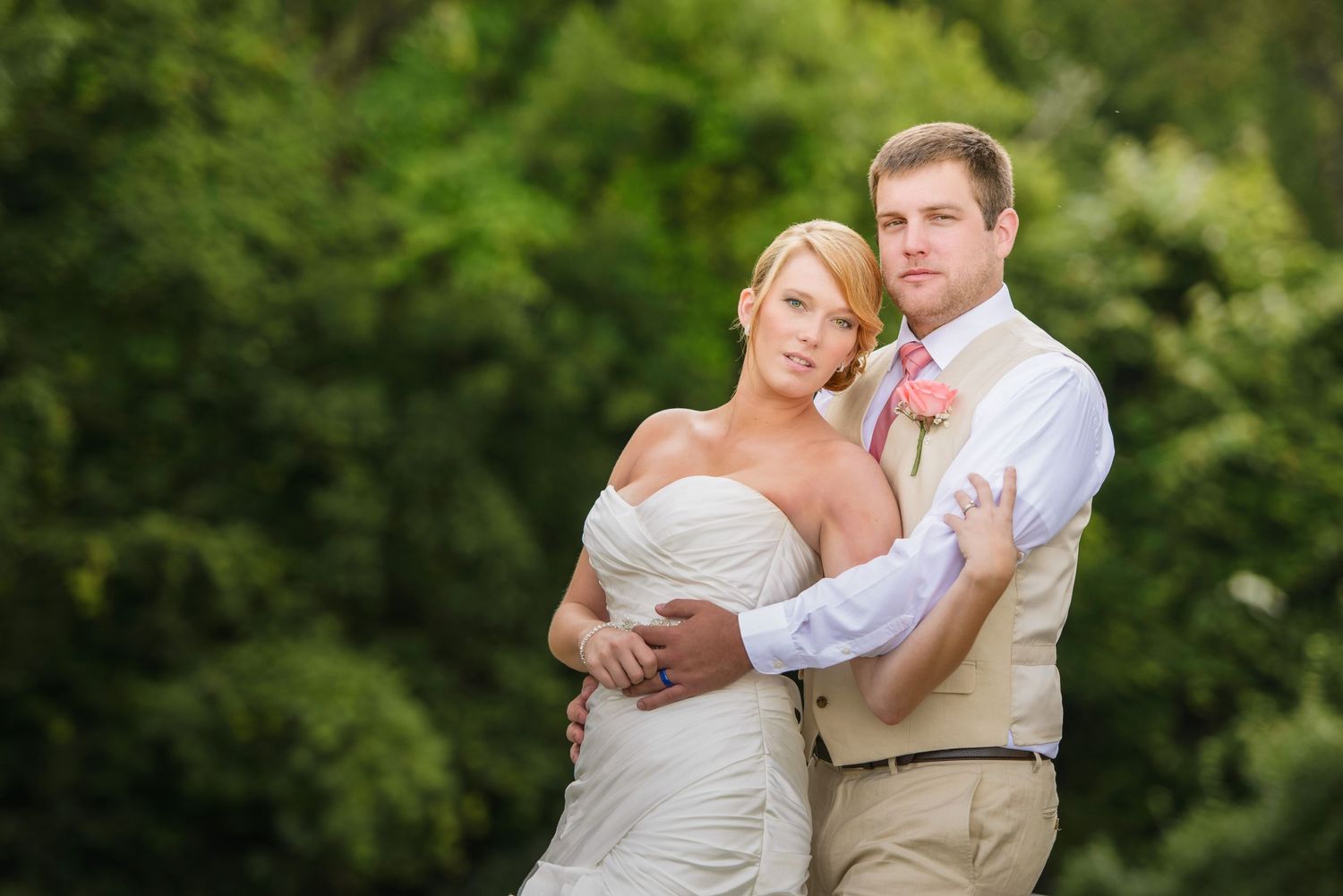 A bride and groom embrace outdoors at a garden wedding with lush green foliage in the background by Gatlinburg TN Wedding Photographers.