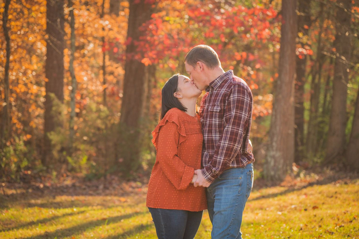 A couple stands close together in a romantic pose surrounded by vibrant fall foliage in golden afternoon light by Gatlinburg TN Photographer