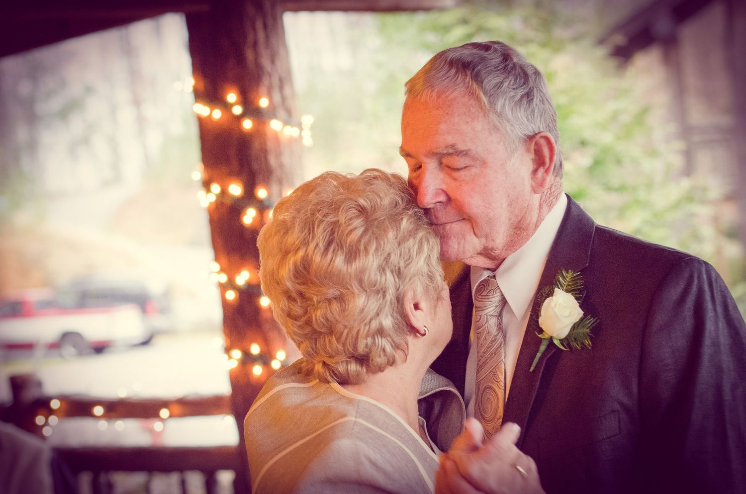 An elderly couple share a tender romantic moment at a wedding reception with twinkling lights in the background in Knoxville TN.